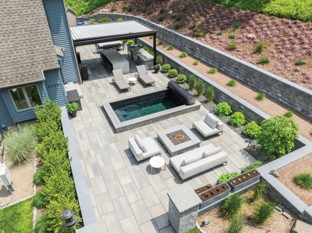 Modern backyard design with Soake Pool, fire pit, patio, louvered pergola, landscaping, and outdoor kitchen built by Bahler Brothers in Burlington, Connecticut