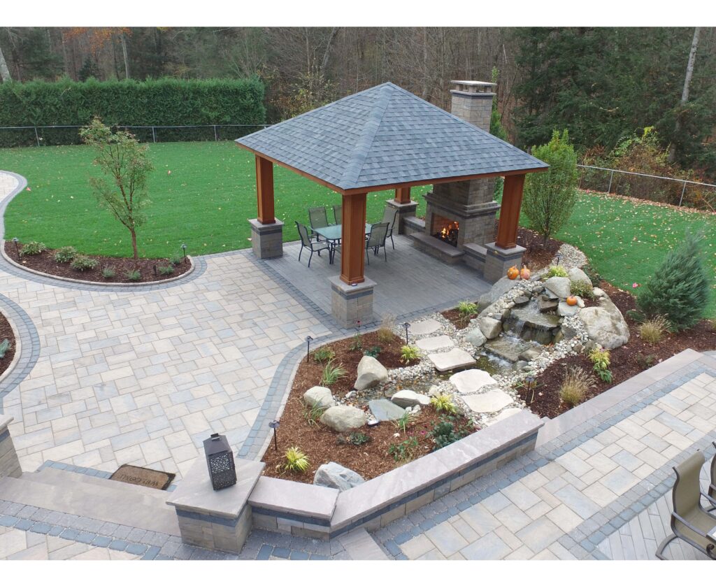 Custom patio design with pavilion, outdoor fireplace, landscape lighting, retaining wall, sitting wall, steps, landscape design, and natural waterfall feature built by Bahler Brothers