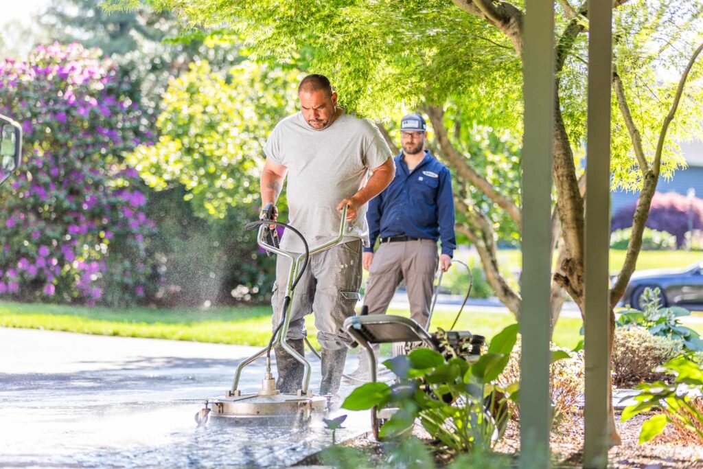 Bahler Brothers crew performing hardscape cleaning and power washing services on a paver walkway using a surface cleaner