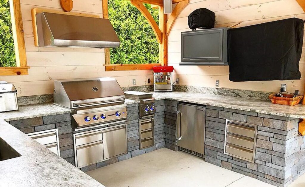 Outdoor kitchen inside covered area with cabinets, fridge, and gas grill built by Bahler Brothers