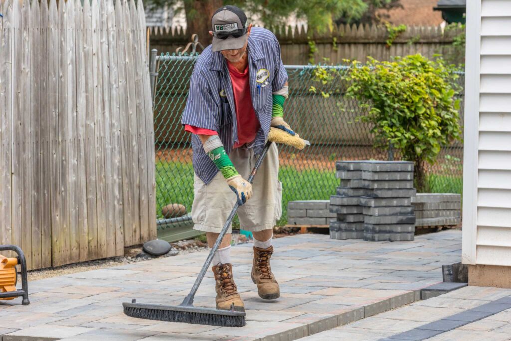 Bahler Brothers crew member sweeping polymeric sand into joints during paver walkway and driveway installation