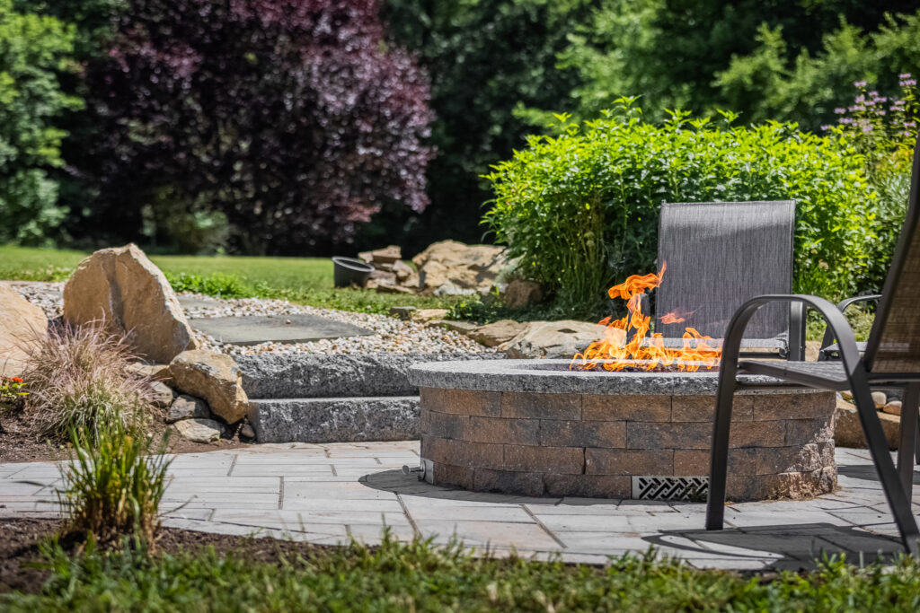 gas a fire pit on a patio with recliner chairs and landscaping